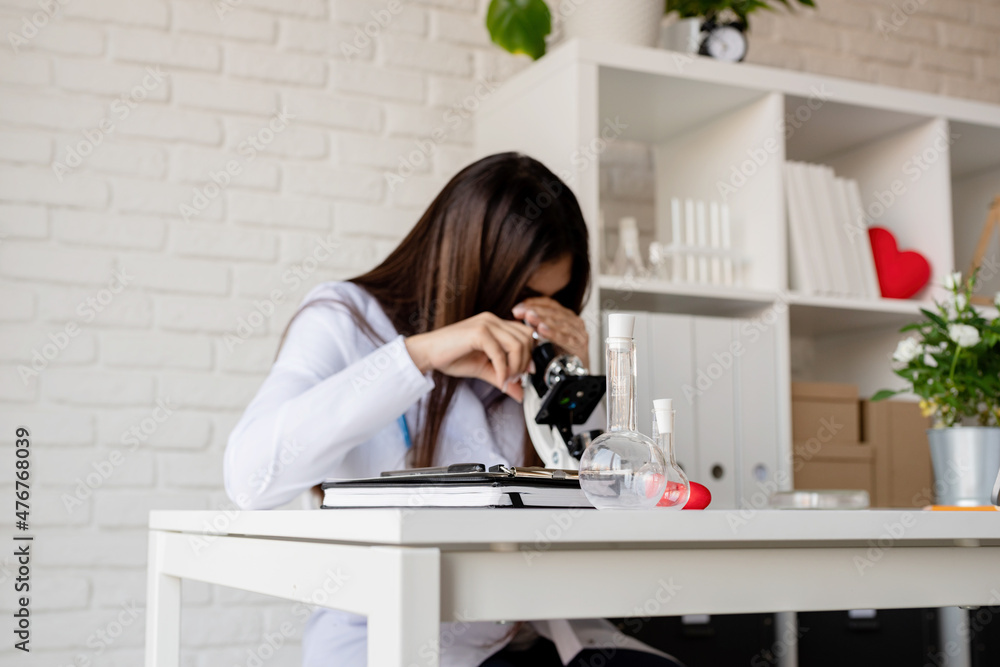 Young doctor or scientist woman using microscope on the background. Test tunes on the desk Young doctor or scientist woman using microscope on the background. Test tunes on the desk