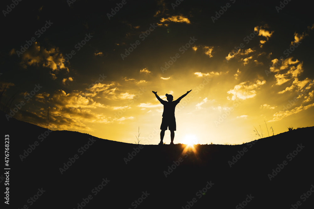 The silhouette of a man raising his hands in freedom on the mountain.