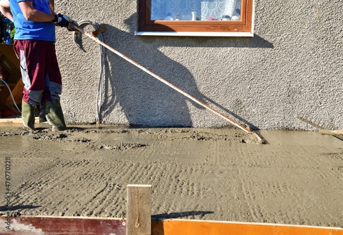 The mason balances and strokes the freshly poured concrete into the plane