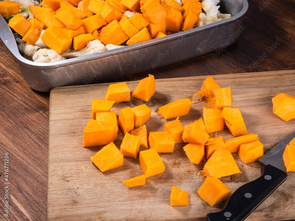 Cooking vegetables with pumpkin in a metal baking sheet - vegetables in a baking sheet and pieces of raw pumpkin on a cutting board close-up