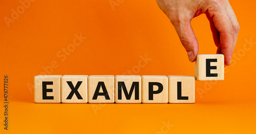 Example symbol. The concept word Example on wooden cubes. Beautiful orange table, orange background, copy space. Businessman hand. Business and example concept.