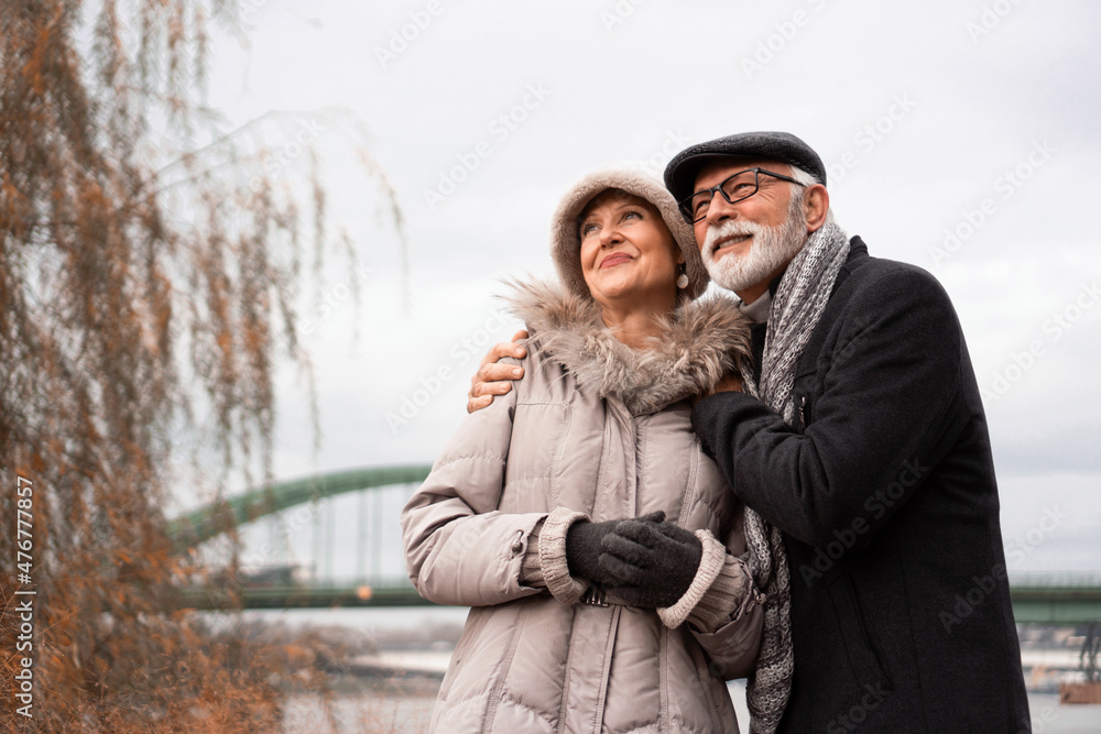 An elderly couple is walking around the waterfront in an urban area. The couple is smiling and looking happy in love. An elderly couple is walking around the waterfront in an urban area. The couple is smiling and looking happy in love.