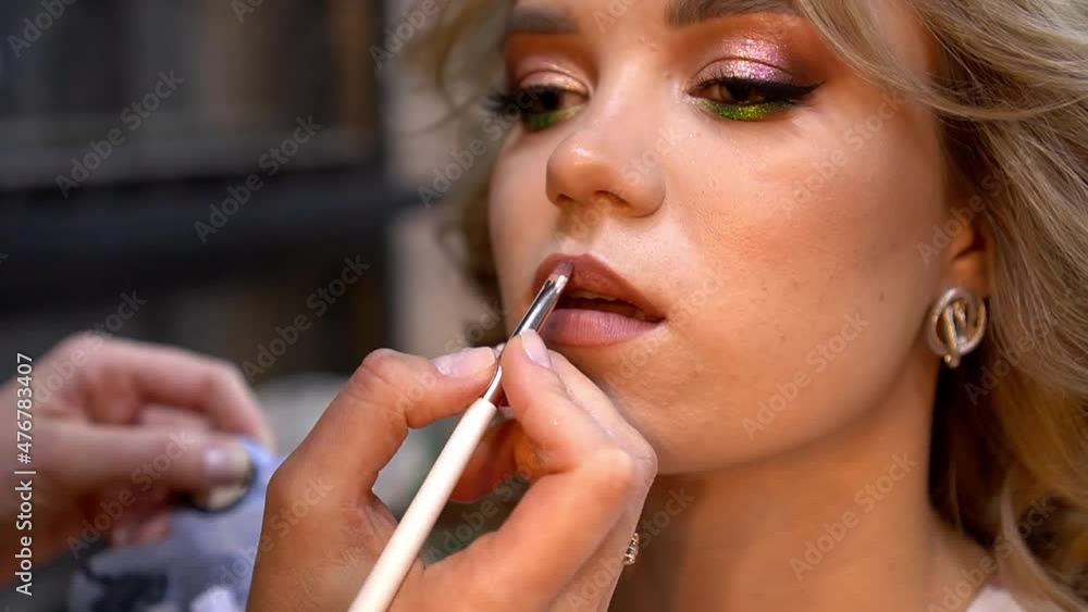 Professional make-up artist applies lipstick with special brush young woman. Close up Professional make-up artist applies lipstick with special brush young woman. Close up