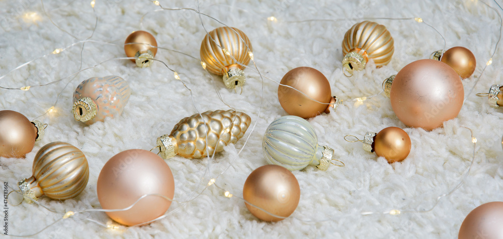 New Year's toys on a white carpet. Golden Christmas tree decorations are scattered on the carpet next to a glowing yellow garland New Year's toys on a white carpet. Golden Christmas tree decorations are scattered on the carpet next to a glowing yellow garland