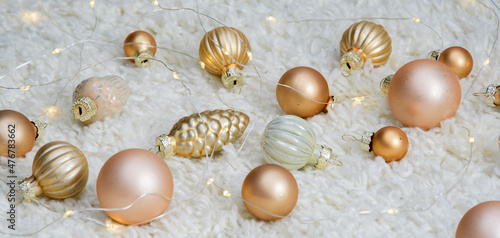 New Year's toys on a white carpet. Golden Christmas tree decorations are scattered on the carpet next to a glowing yellow garland