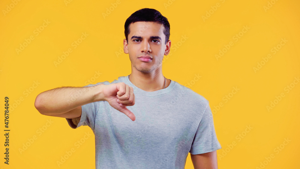 young man in t-shirt showing dislike isolated on yellow. young man in t-shirt showing dislike isolated on yellow.