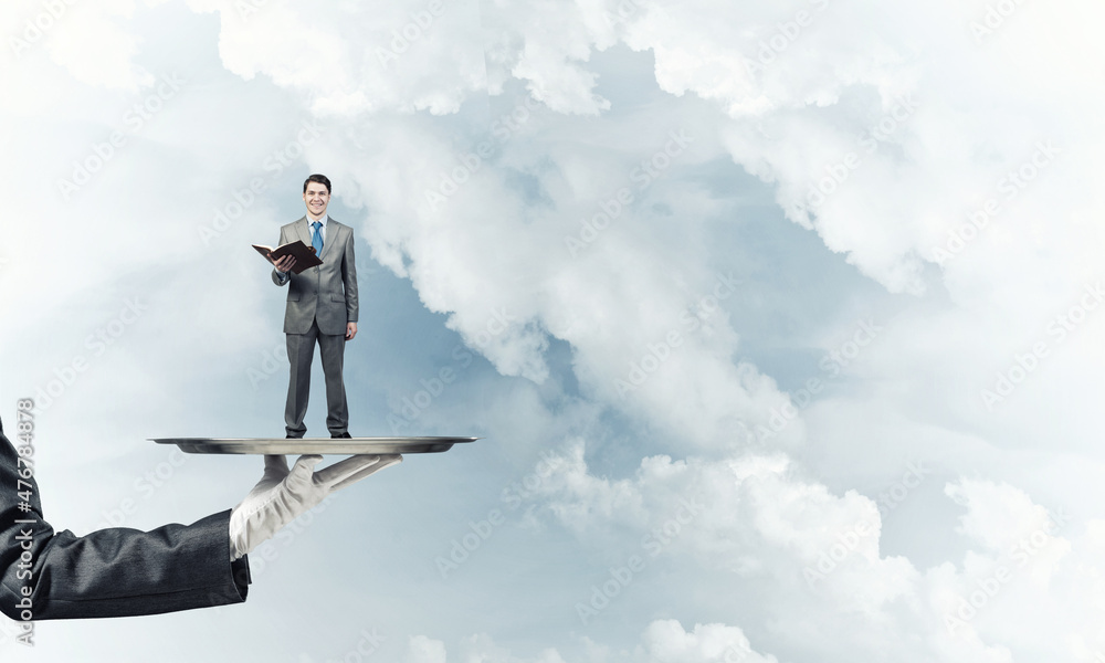 Businessman on metal tray with red book in hands against blue sky background Businessman on metal tray with red book in hands against blue sky background
