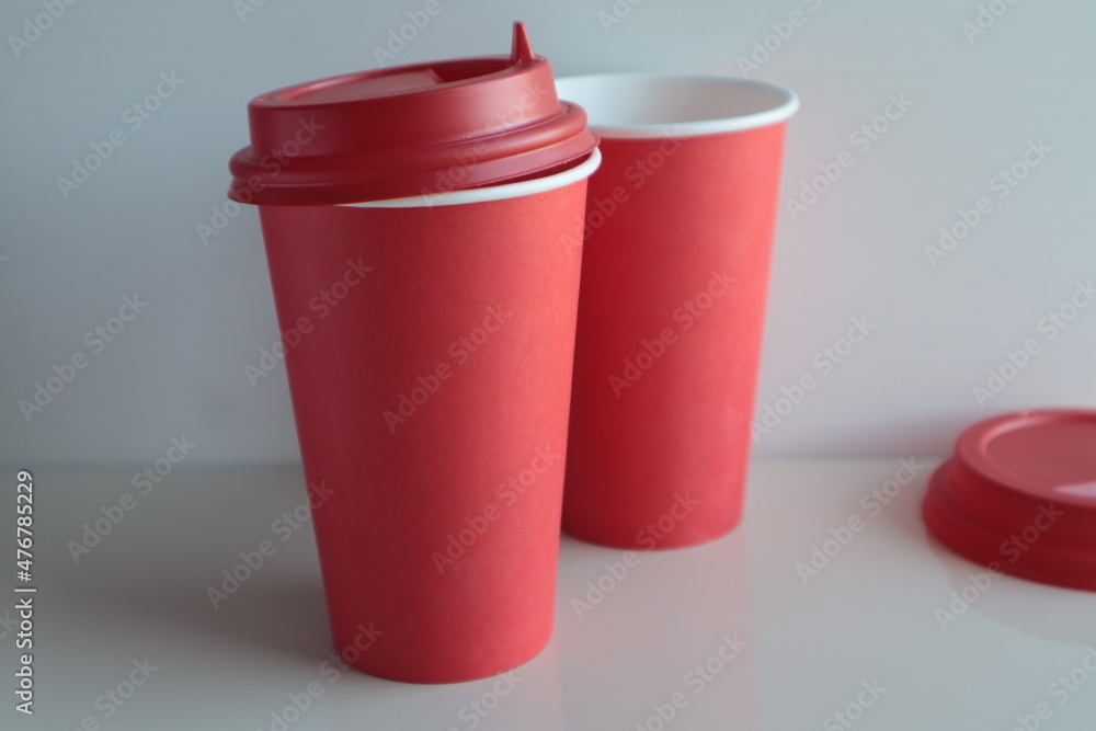 Red paper disposable cups stand on a light surface. Red paper disposable cups stand on a light surface.
