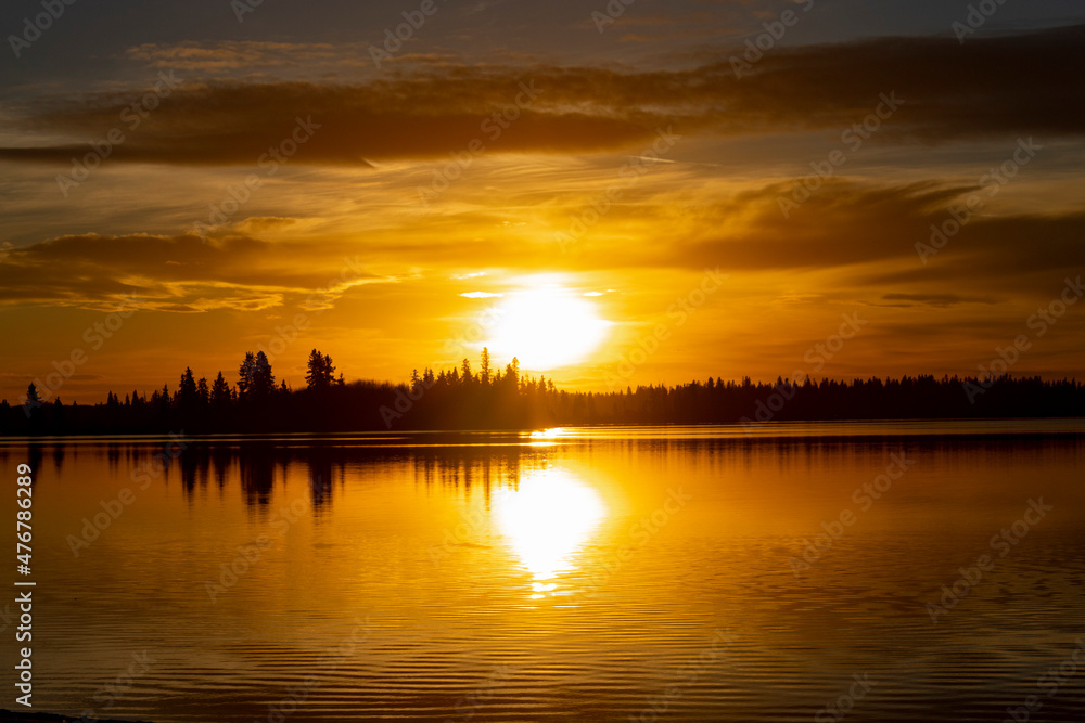 Orange and Yellow sunset over lake with Black silhouetted tree line