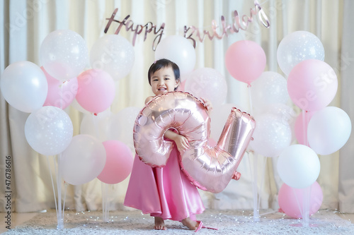 Asian cute little girl in a beautiful pink dress holding the balloon and celebrating her second birthday in the party at home.