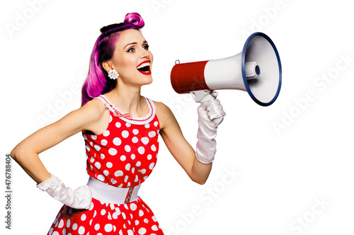 Beauty red haired woman holding megaphone, shout something. Girl in pinup style dress in polka dot, isolated over white background. Pin up model posing in retro fashion vintage concept.