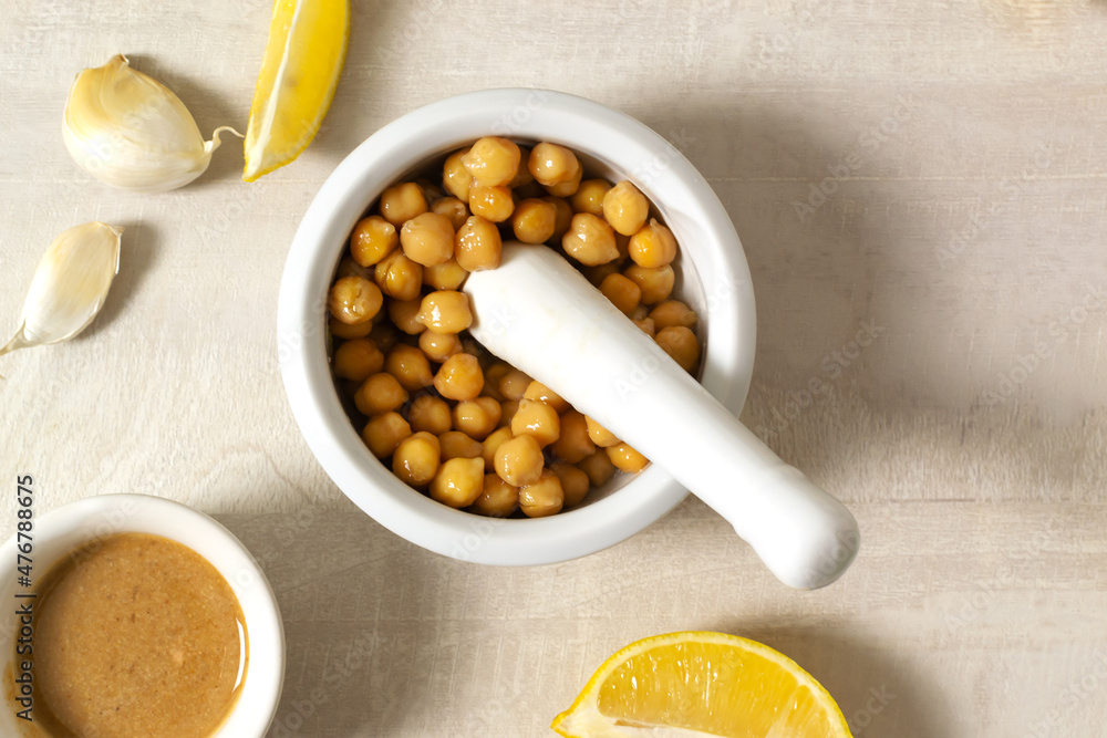 Add boiled chickpeas to Garlic with lemon juice in a ceramic mortar. Ingredients for making hummus. Boiled chickpeas, tahini, garlic, lemon and butter. A traditional Middle Eastern dish. Top view. Add boiled chickpeas to Garlic with lemon juice in a ceramic mortar. Ingredients for making hummus. Boiled chickpeas, tahini, garlic, lemon and butter. A traditional Middle Eastern dish. Top view.