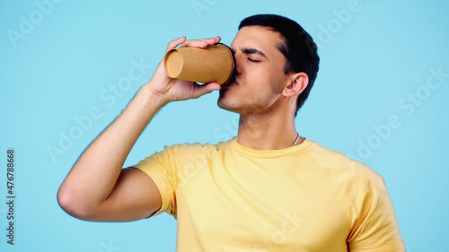 young man with closed eyes drinking coffee to go isolated on blue.