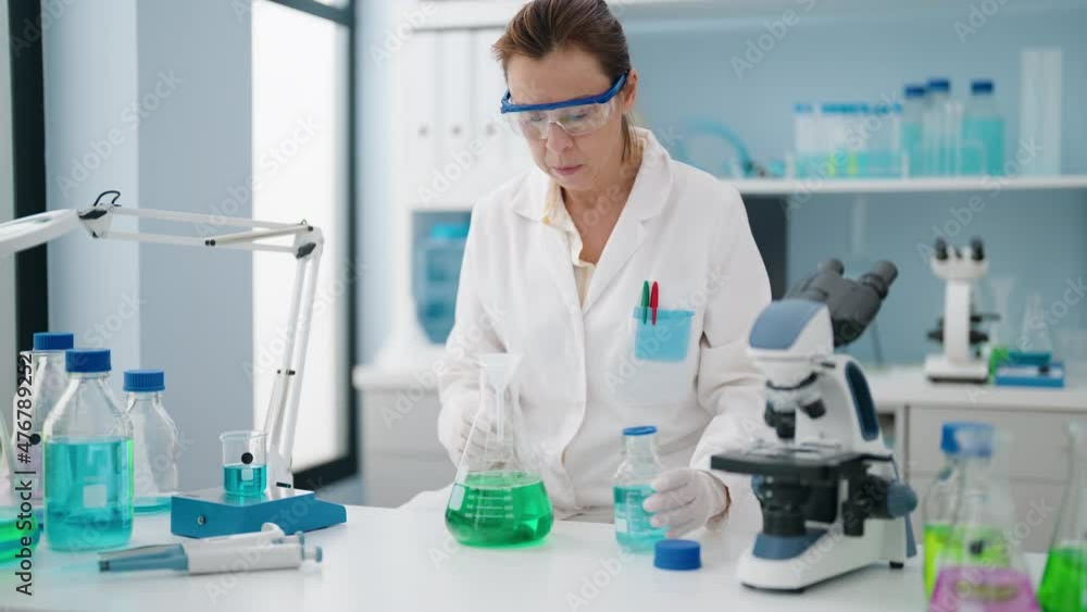 Middle age woman wearing scientist uniform measuring liquid at laboratory Middle age woman wearing scientist uniform measuring liquid at laboratory