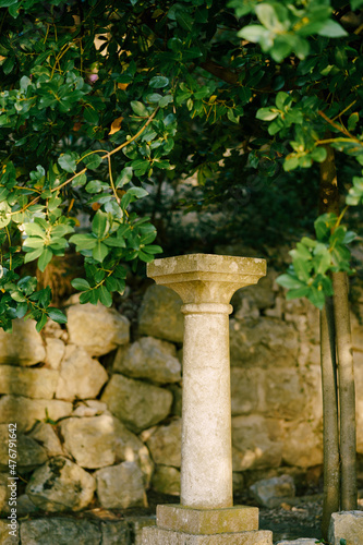 Simple stone column in the garden near the stone wall