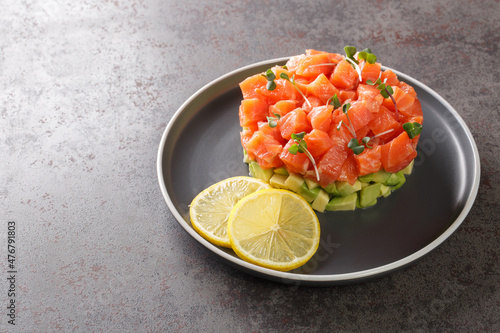 Salmon tartare with slices of avocado, served with lemon and microgreen on grey stone board photo