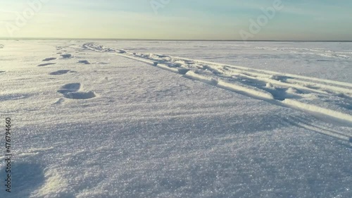 The drone flies over a snowy lake. Shiny snow flies around. The drone hovers over a snowy field. A hovercraft rides on a snow-covered lake.