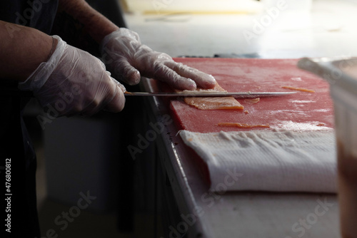 Сook cuts the red fish into very thin pieces with a sharp knife.