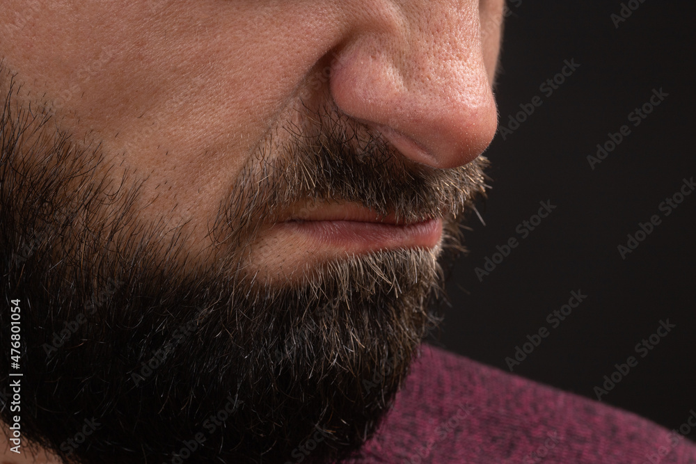 Obraz premium wrinkled grimace of danger, closeup on face and lips of young unrecognizable man with black beard and mustache, concept of rage and anger.