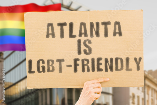 The phrase " Atlanta is LGBT-Friendly " on a banner in men's hand with blurred LGBT flag on the background. Human relationships. different. Diverse. liberty. Sexuality. Social issues. Society