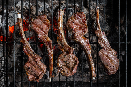 Grilled lamb mutton chop steaks on barbecue, outdoor BBQ grill with fire. Top view