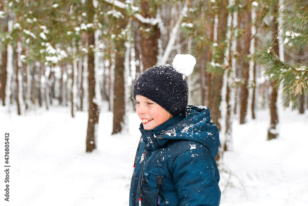 Defocus smiling child boy in winter forest in snowstorm with snowball on head. Funny kid standing near tree on snowy winter background. Actively spending time outdoors. Out of focus Defocus smiling child boy in winter forest in snowstorm with snowball on head. Funny kid standing near tree on snowy winter background. Actively spending time outdoors. Out of focus