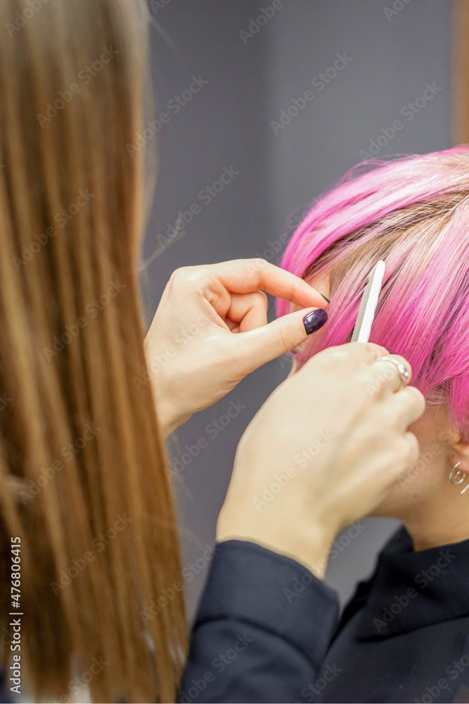Fototapeta premium Hairdresser prepares dyed short pink hair of a young woman to procedures in a beauty salon