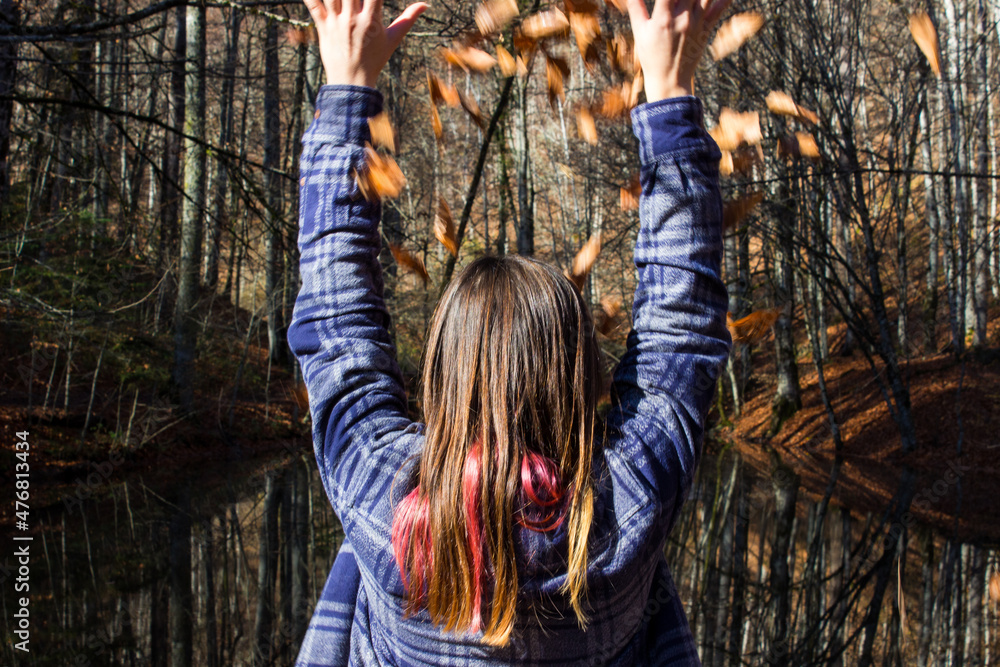 Person in the forest. Woman in the forest in autumn season and throwing autumn leaves around arms wide open. Woman greeting the autumn fall season. Free woman enjoying the seasonal changes.