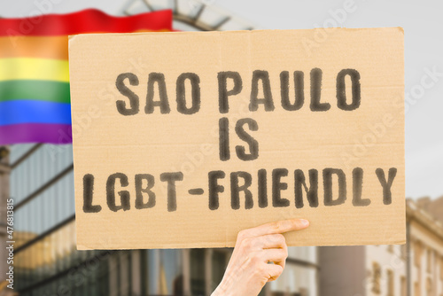 The phrase " Sao Paulo is LGBT-Friendly " on a banner in men's hand with blurred LGBT flag on the background. Human relationships. different. Diverse. liberty. Sexuality. Social issues. Society