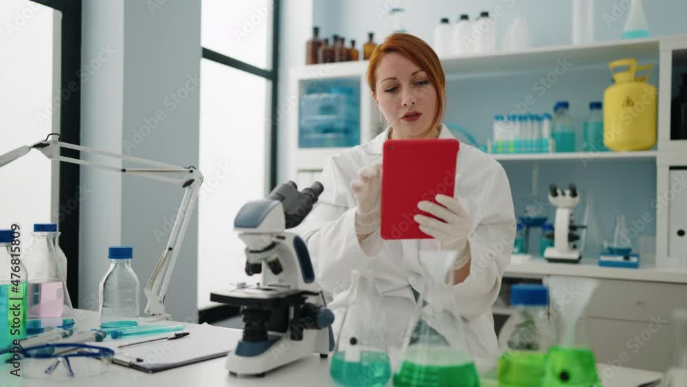 Young redhead woman wearing scientist uniform using touchpad at laboratory Young redhead woman wearing scientist uniform using touchpad at laboratory