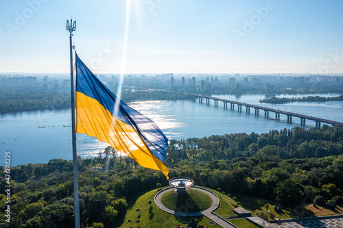 Aerial view of the Ukrainian flag waving in the wind against the city of Kyiv, Ukraine near the famous statue of Motherland.