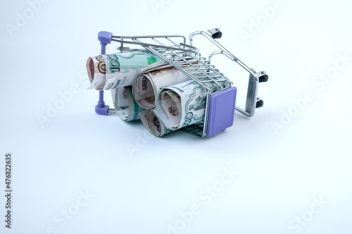 Financial still life: an inverted grocery iron cart with Russian money on a light background