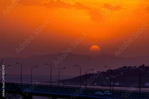 Bright sunset in Vladivostok. The red sun sets on the hills against the background of the road and the sea.