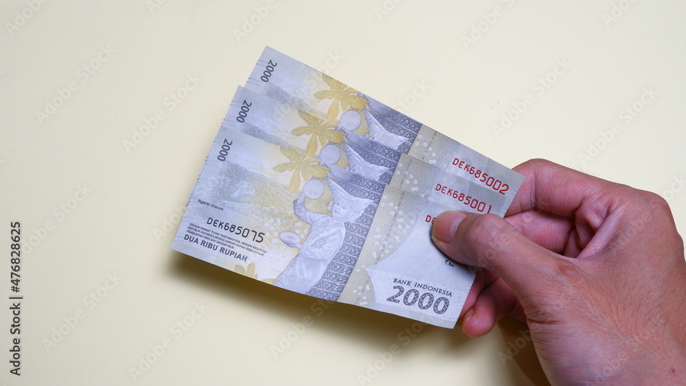 A man's hand is making a payment. Male hand showing Indonesian rupiah note. Indonesian Rupiah the official currency of Indonesia. Business and finance concept. Uang 2000 Rupiah.