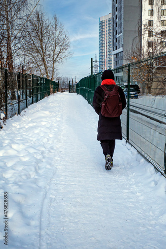Fototapeta Naklejka Na Ścianę i Meble -  A man with a backpack walks along a snow-covered sidewalk on a winter day