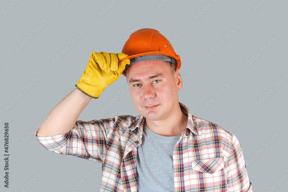 Portrait of a working man in an orange helmet and gloves, a worker holding a helmet with his hand looking at the camera. Portrait of a working man in an orange helmet and gloves, a worker holding a helmet with his hand looking at the camera.