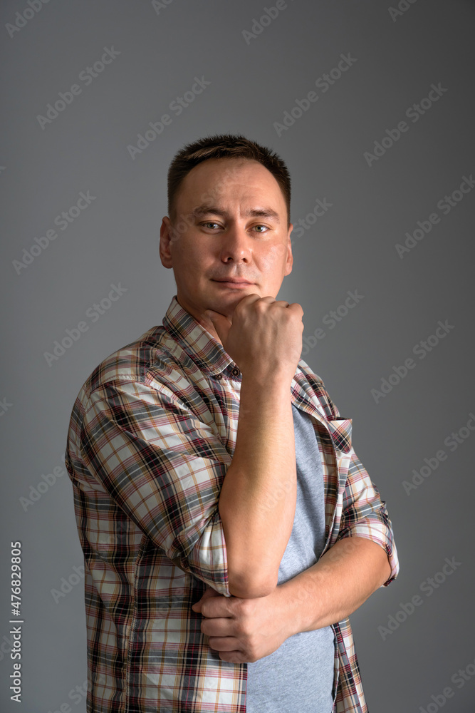 Portrait of a 30s man in casual clothes holding his hand on his chin on a gray background, close-up Portrait of a 30s man in casual clothes holding his hand on his chin on a gray background, close-up