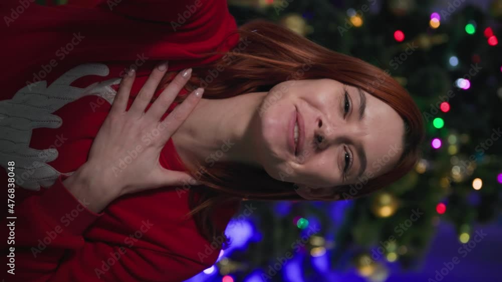 mobile camera vertical view, beautiful girl in red sweater with a deer congratulates online happy new year on the background of a blinking christmas tree at home mobile camera vertical view, beautiful girl in red sweater with a deer congratulates online happy new year on the background of a blinking christmas tree at home