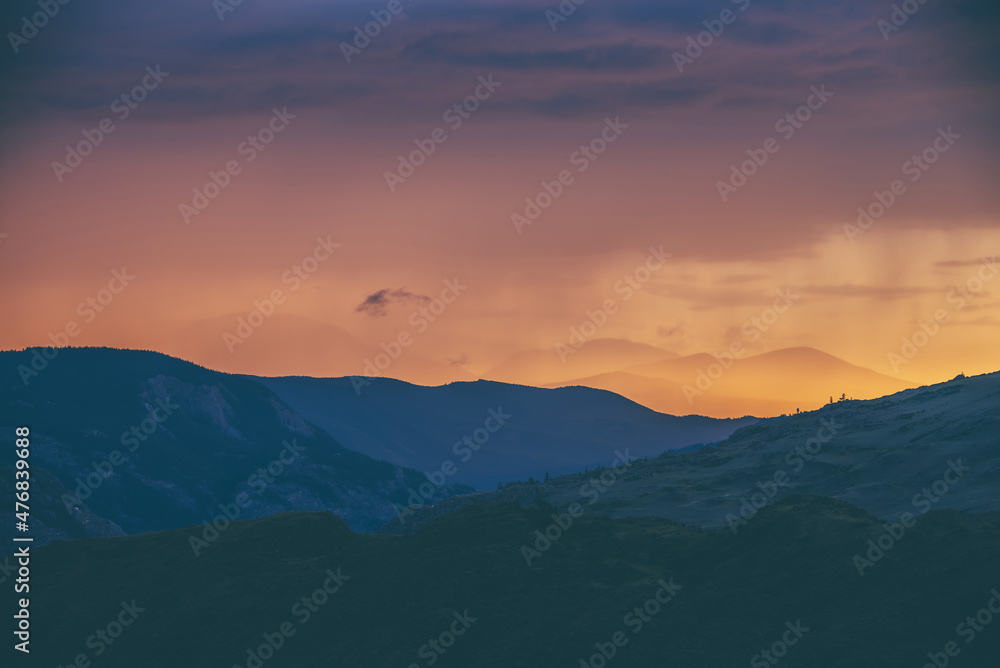 Atmospheric landscape with silhouettes of mountains with trees on background of vivid orange blue lilac dawn sky. Colorful nature scenery with sunset or sunrise of illuminating color. Sundown paysage.
