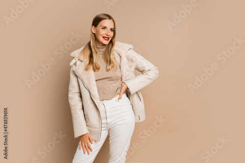Pretty legant blond woman with red lips wearing trendy eco leather jacket , posing over beige background. Winter fashion trends.