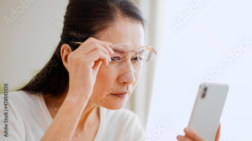 老眼鏡でスマートフォンを覗くシニア女性 photo