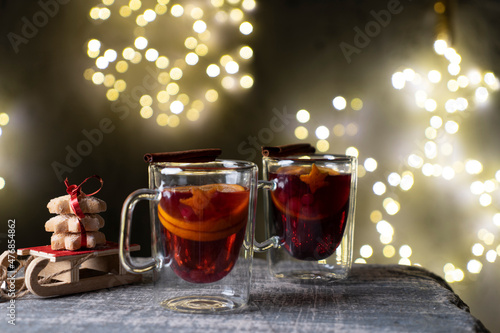 Festive mulled wine with spices, sledges and cookies on a background of bright lights