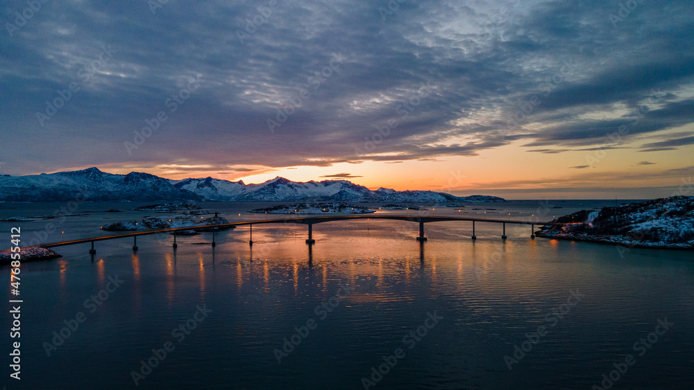 Bridge in Norway between two islands with snowy mountains and the Sunset in the background - Drone Perspective Landscape Photography