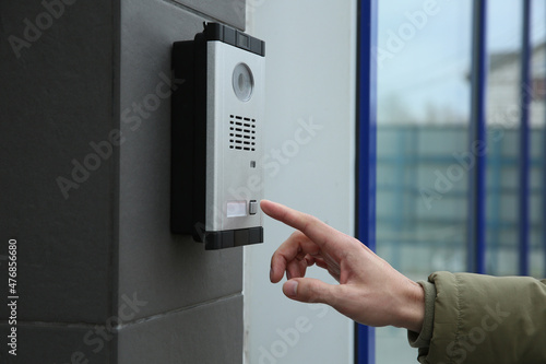 Man ringing intercom with camera near building entrance, closeup