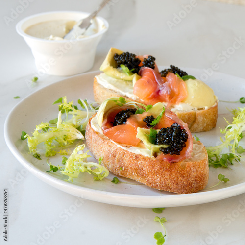 a plate of bruschetta with cream cheese, avocado, salmon and black caviar on a light table photo