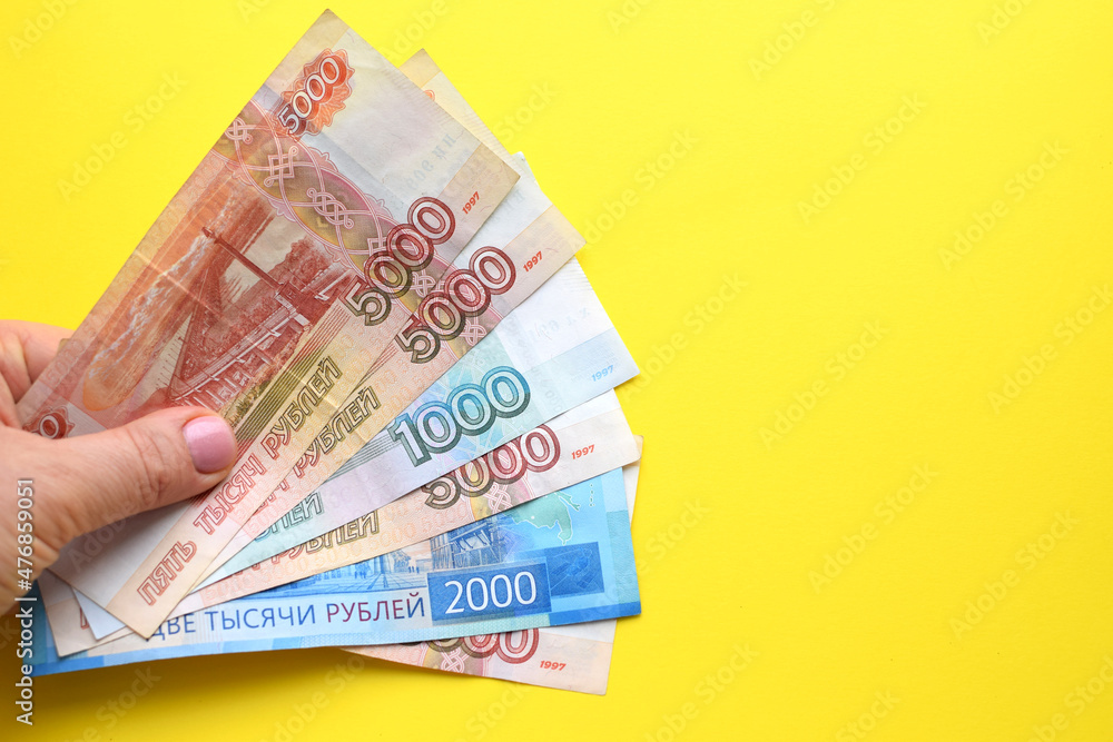 Obraz premium Russian ruble banknotes in a female hand on a yellow background.