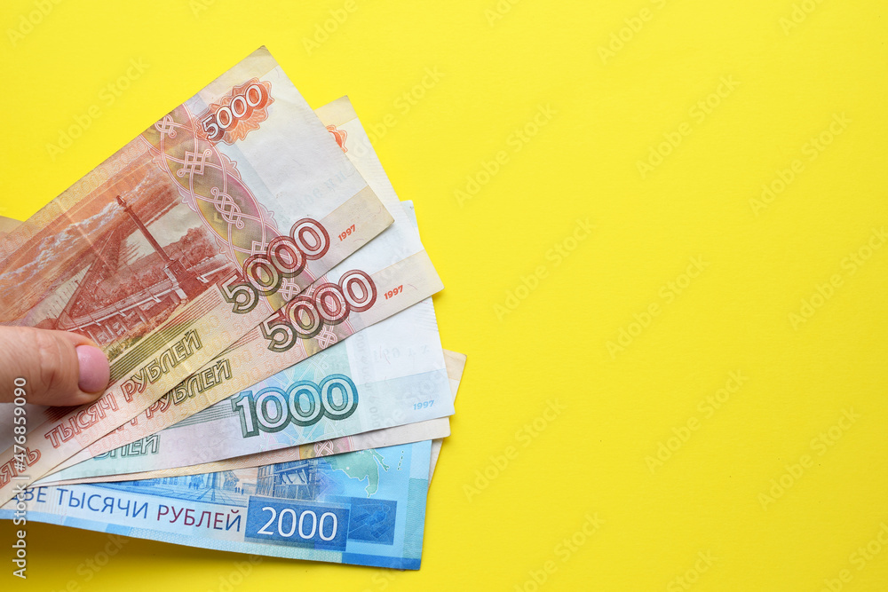 Obraz premium Russian ruble banknotes in a female hand on a yellow background. Copy space.