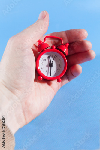 A man's hand holds a red small alarm clock on a blue background