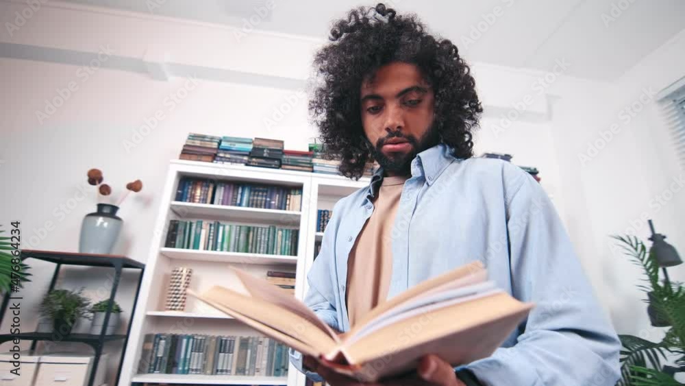 Carried away young inquisitive Indian man stands with book in hands carefully reading textbook to improve skills in something or studying business literature. Education university, learning and people Carried away young inquisitive Indian man stands with book in hands carefully reading textbook to improve skills in something or studying business literature. Education university, learning and people