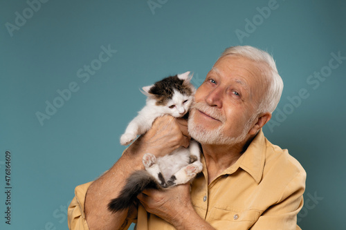 A man with gray hair holding a little kitten in her hands, a love concept for animals, on a blue background, an empty space for text